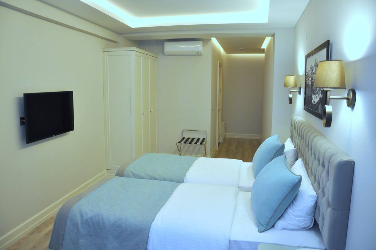 A hotel room with a bed, a television, a wardrobe, an air conditioning unit, and a hallway leading to another room.