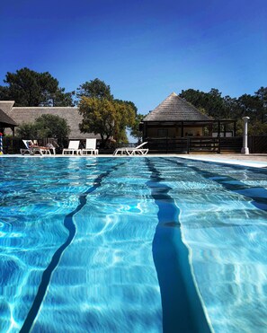 Una piscina cristalina con sillones de descanso y un pabellón al fondo.