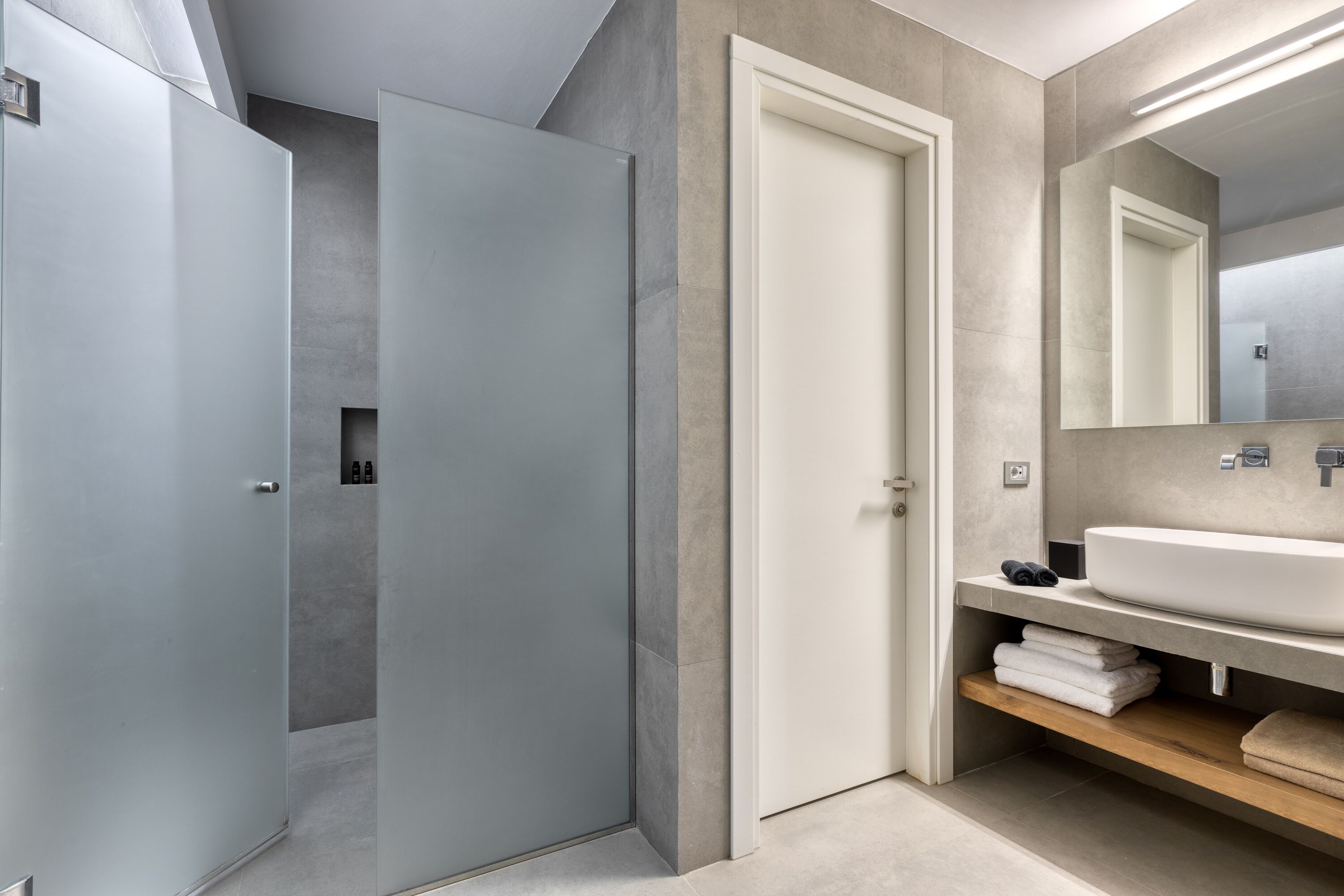 Un bagno moderno con uno specchio grande, un lavandino bianco e uno scaffale in legno.