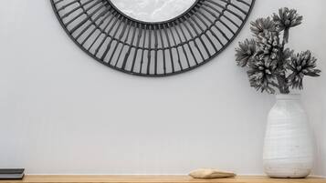 A modern room with a round mirror, a wooden desk, a white vase with flowers, and a wooden chair.
