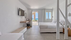 A modern bedroom with a bed, a desk, and a TV. There is a view of the beach through an open door. - Elia Mykonos Resort (Mykonos)