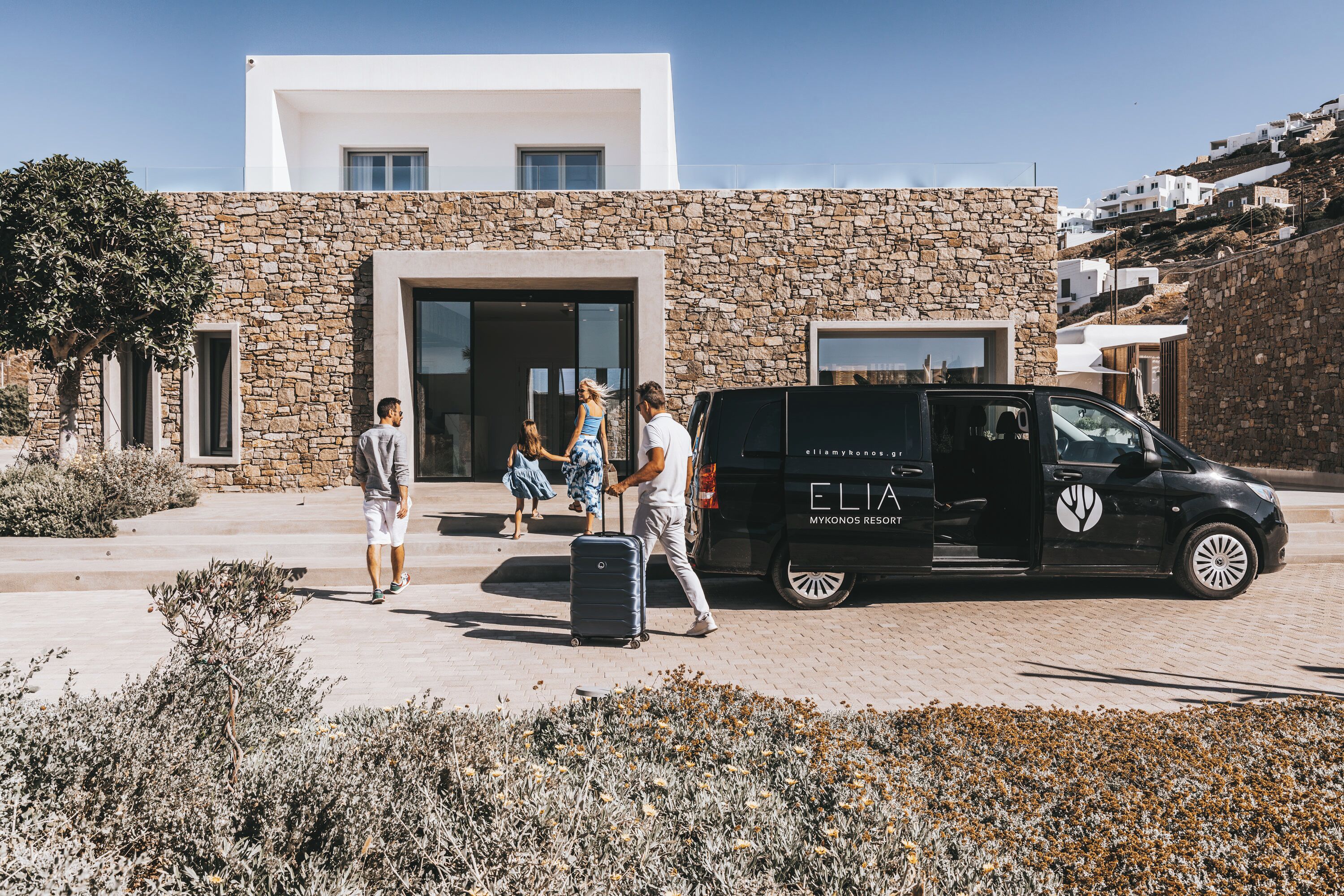 A stone building with a modern design, a black van with 'ELIA' branding, and a clear sky.