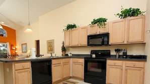 A modern kitchen with wooden cabinets, a black microwave, a stove, and a dishwasher. There are plants on the cabinets and a window with curtains. - Ov2348 - Emerald Island Resort - 5 Bed 4.5 Baths Villa (Davenport)