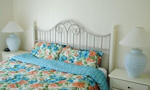 A bed with floral bedding, a metal headboard, and two bedside lamps on white nightstands.