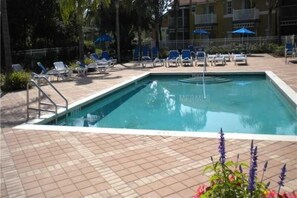 A rectangular swimming pool with a tiled deck, surrounded by lounge chairs and umbrellas.