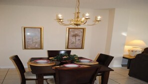 A dining area with a chandelier, two framed pictures, a table set for four, and a side table with a lamp.
