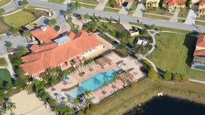 An aerial view of a resort with a swimming pool, palm trees, and a beach area.