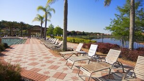 A poolside area with lounge chairs, a tiled walkway, and a body of water.