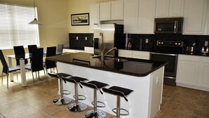 A modern kitchen with white cabinets, stainless steel appliances, and a central island with bar stools.