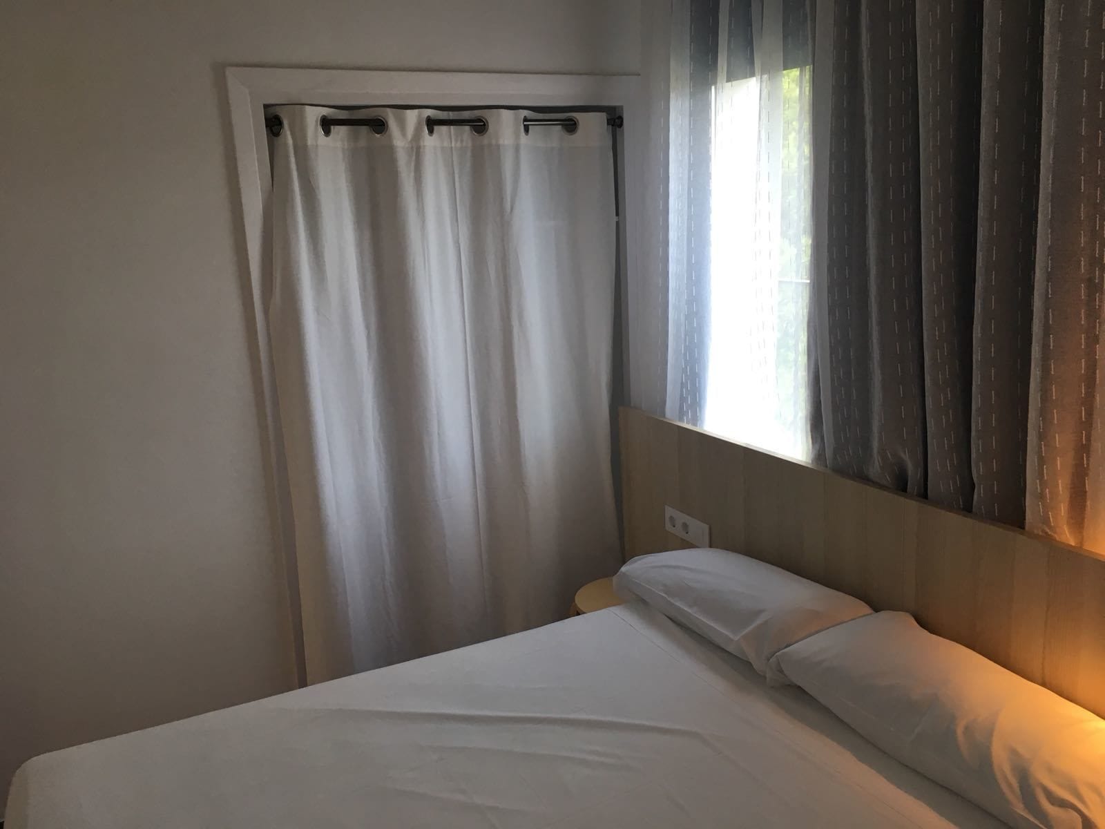 Un dormitorio con una cama, una ventana con cortinas y una lámpara fijada a la pared.
