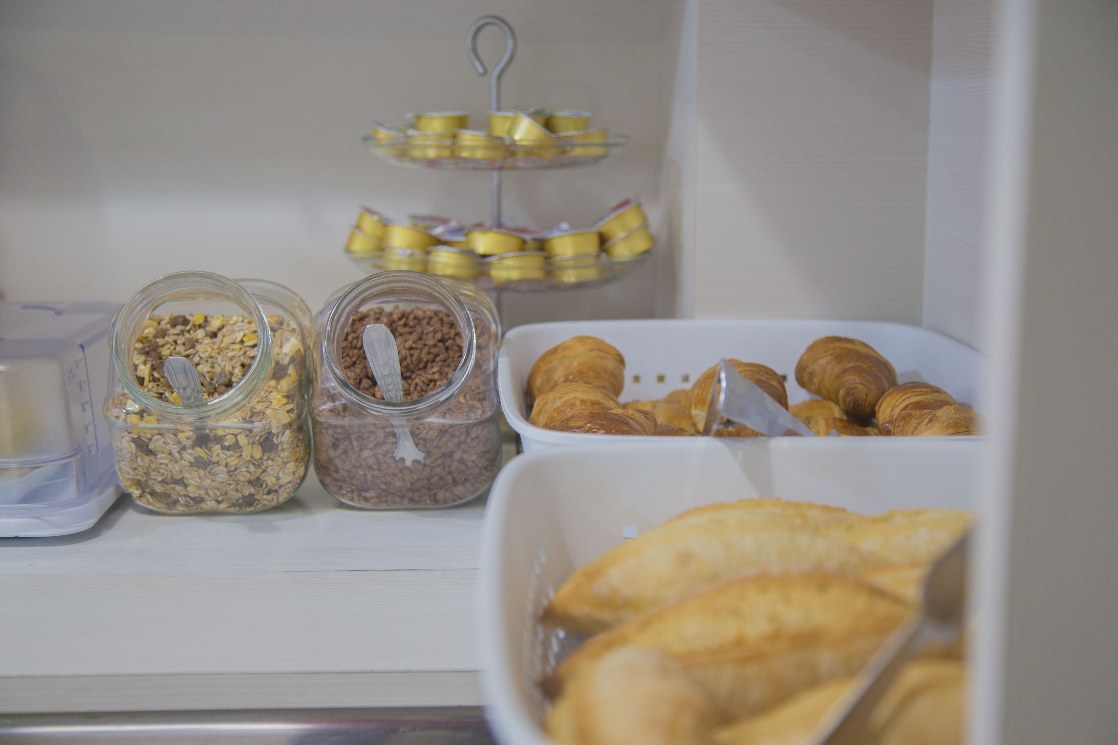 Un frigorifero con diversi alimenti, tra cui vasetti di granola e un vassoio di croissant.