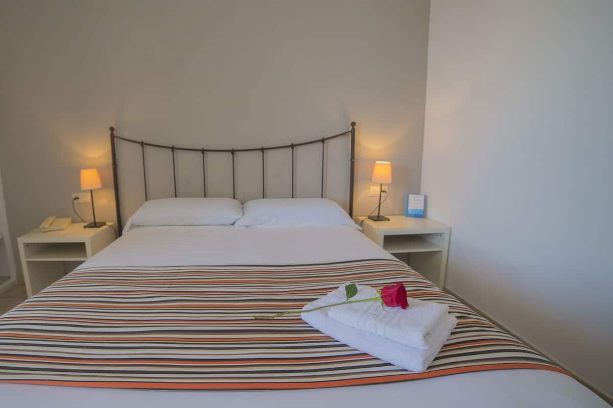 A neatly made bed with a striped bedspread, two bedside lamps, and a folded towel with a rose on a nightstand.