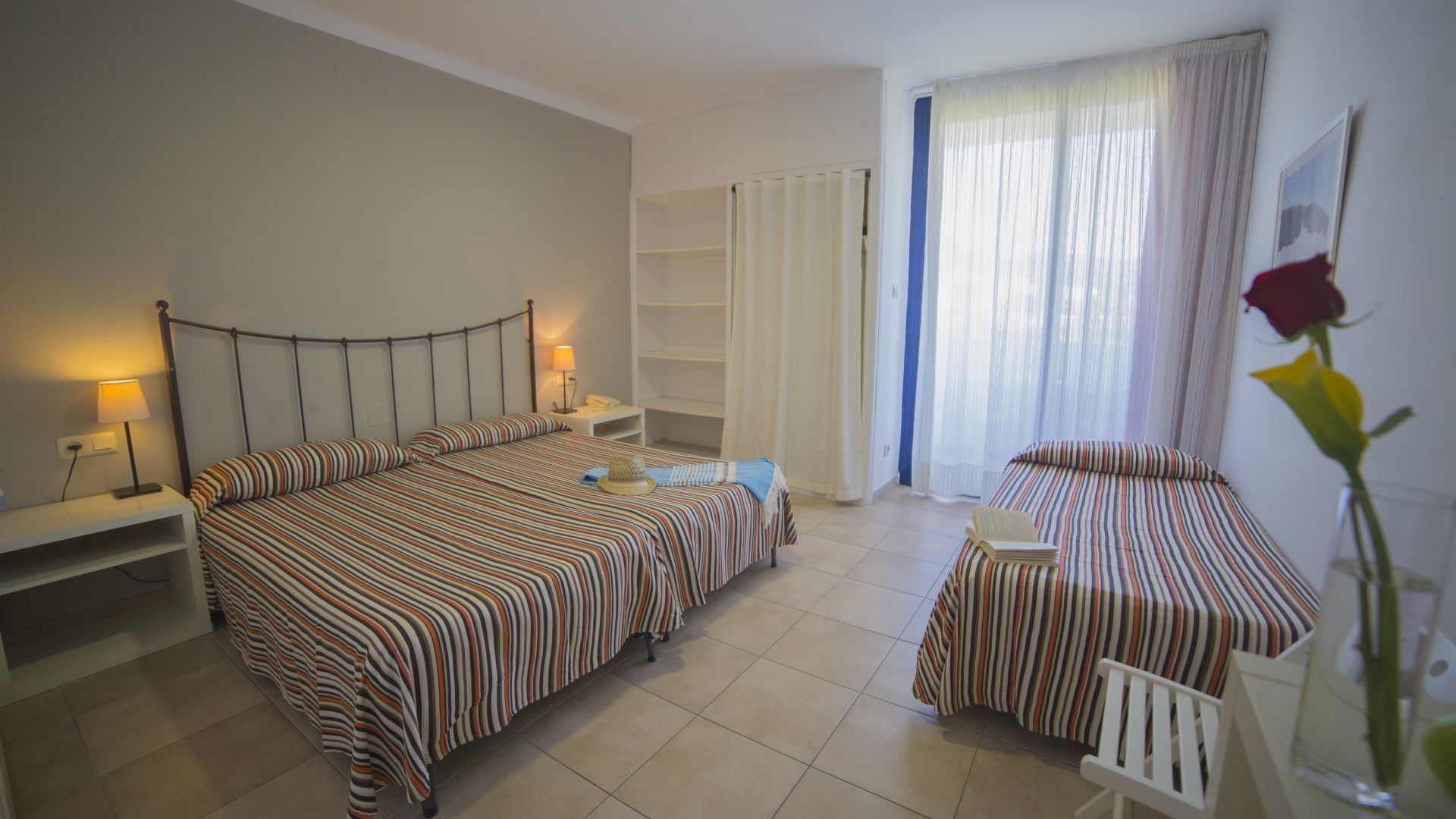 Habitación de hotel con cama doble, una cama individual, escritorio, silla y un ventanal con cortinas.