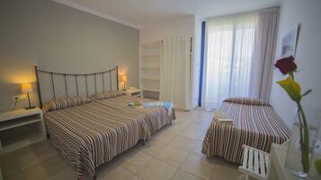Habitación de hotel con cama doble, una cama individual, escritorio, silla y un ventanal con cortinas.