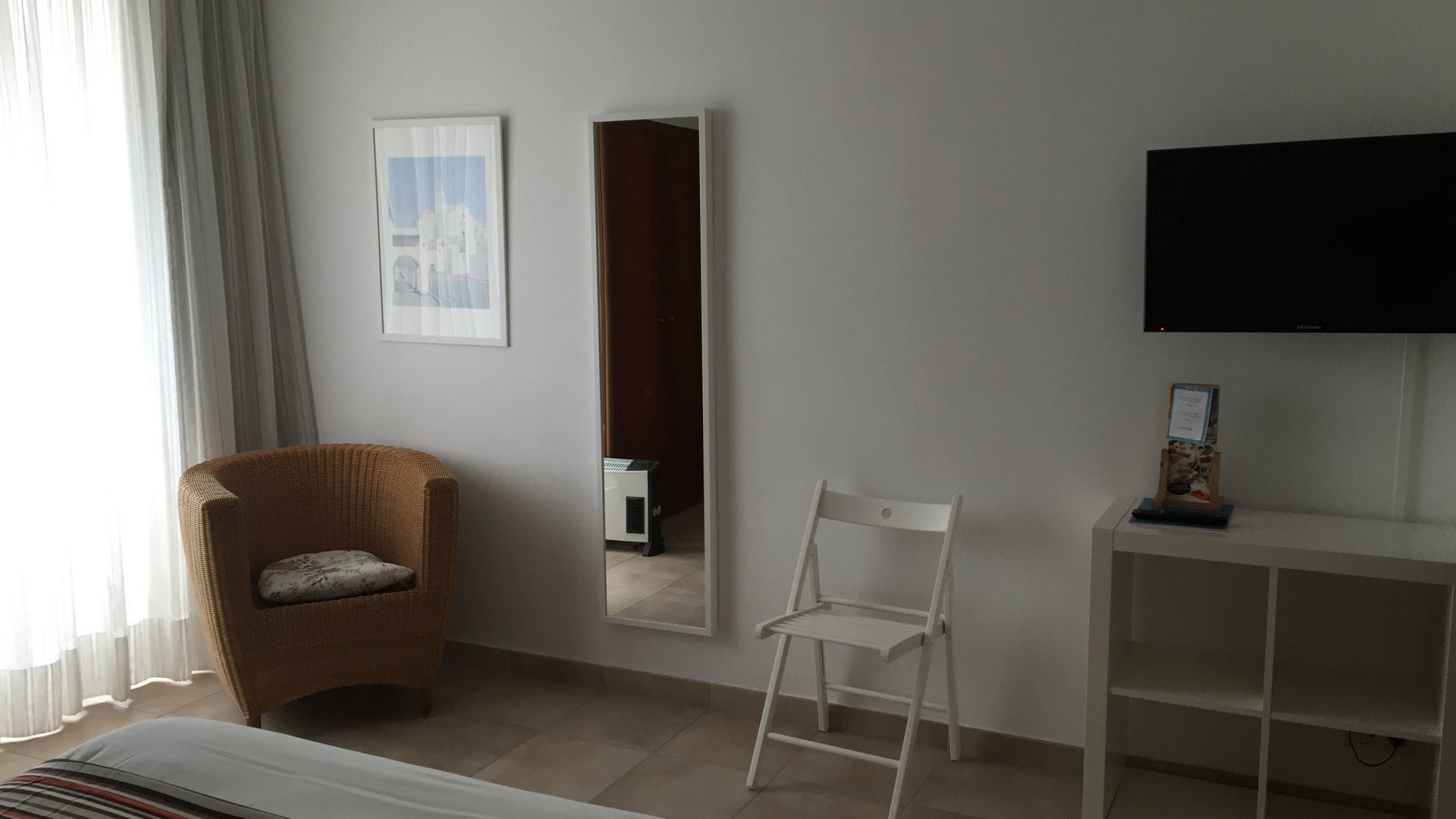 Quarto de hotel com cadeira de vime, cadeira branca, televisão de tela plana e quadro na parede.