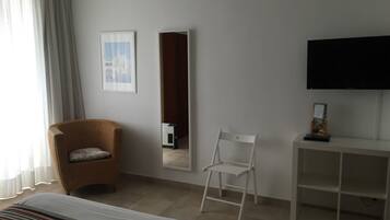 Quarto de hotel com cadeira de vime, cadeira branca, televisão de tela plana e quadro na parede.