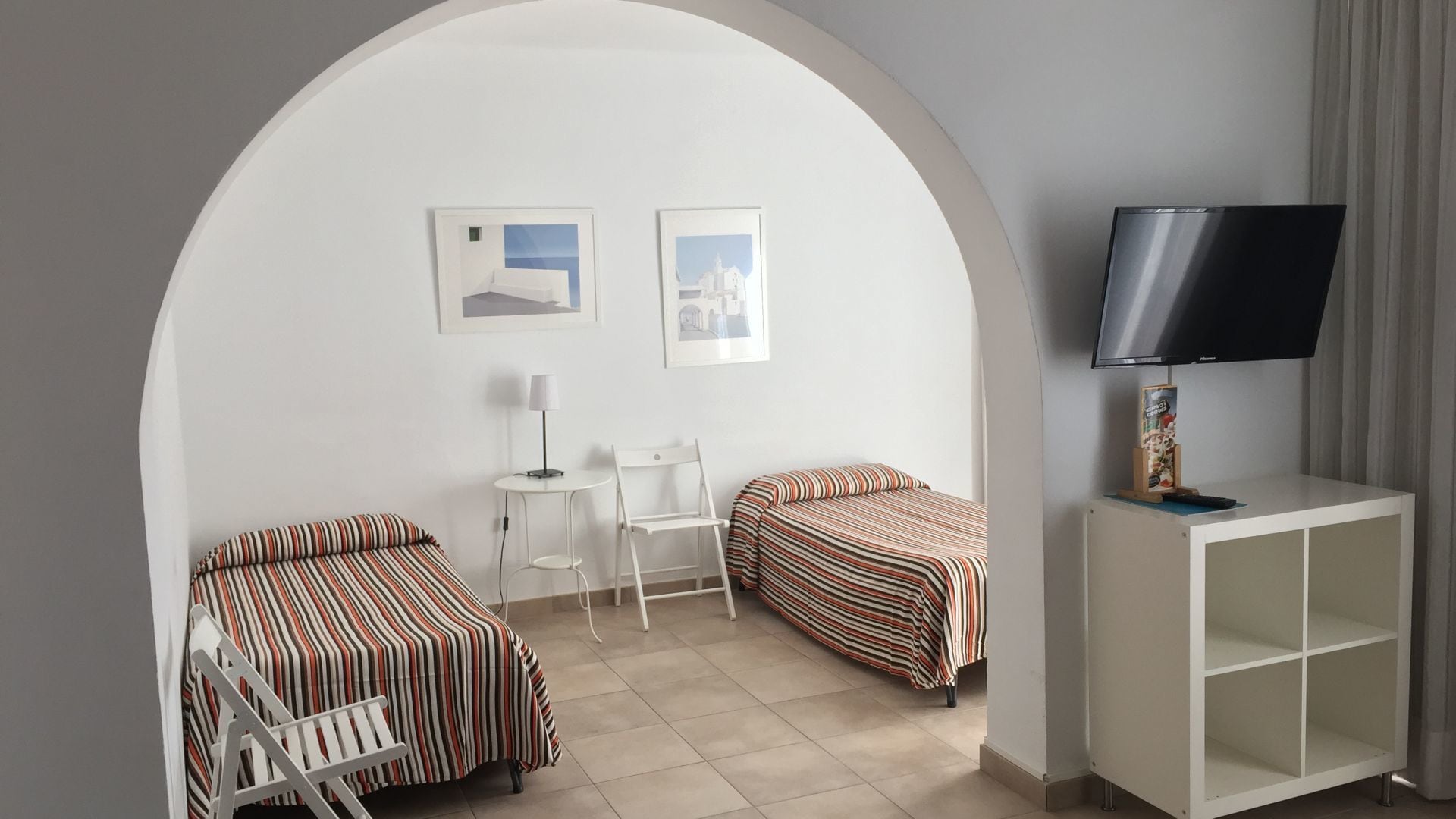A hotel room with two beds, a desk, a chair, a TV, and framed pictures on the wall.