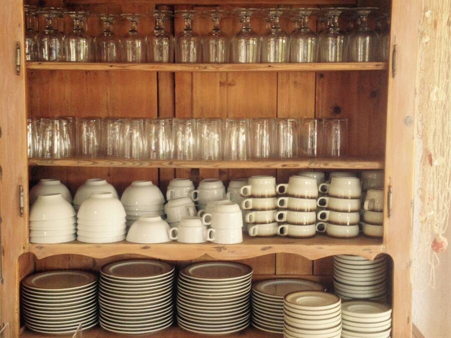 A wooden cabinet with shelves containing glassware, white mugs, and stacked plates.