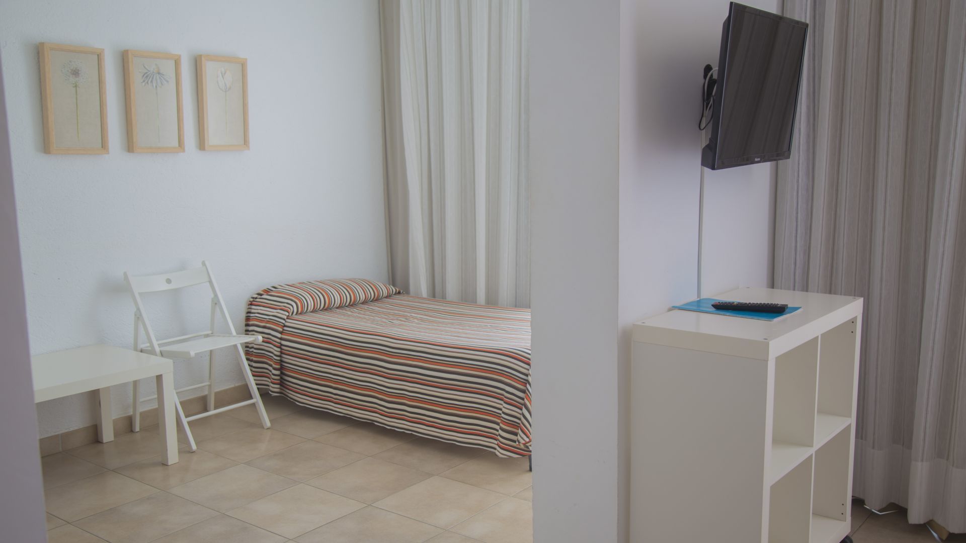 A small, clean room with a bed, a desk, a chair, and a TV mounted on the wall.