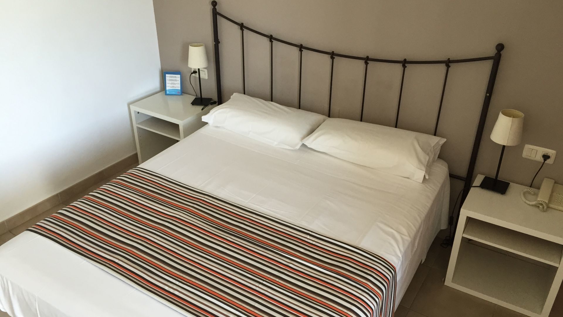 A neatly made bed with white linens, a striped blanket, and two bedside tables with lamps and a phone.