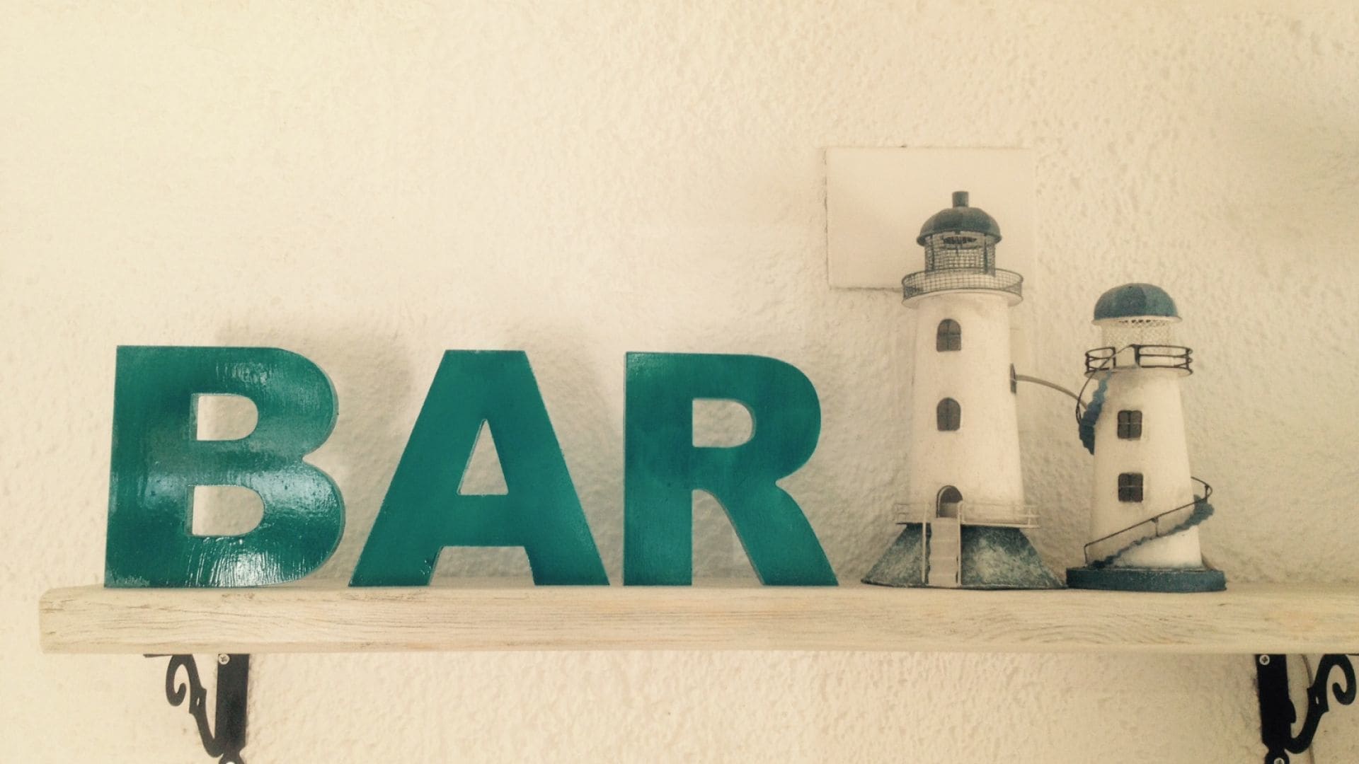 Une étagère sur laquelle est inscrit le mot « BAR » en grandes lettres, deux phares et un petit objet carré.