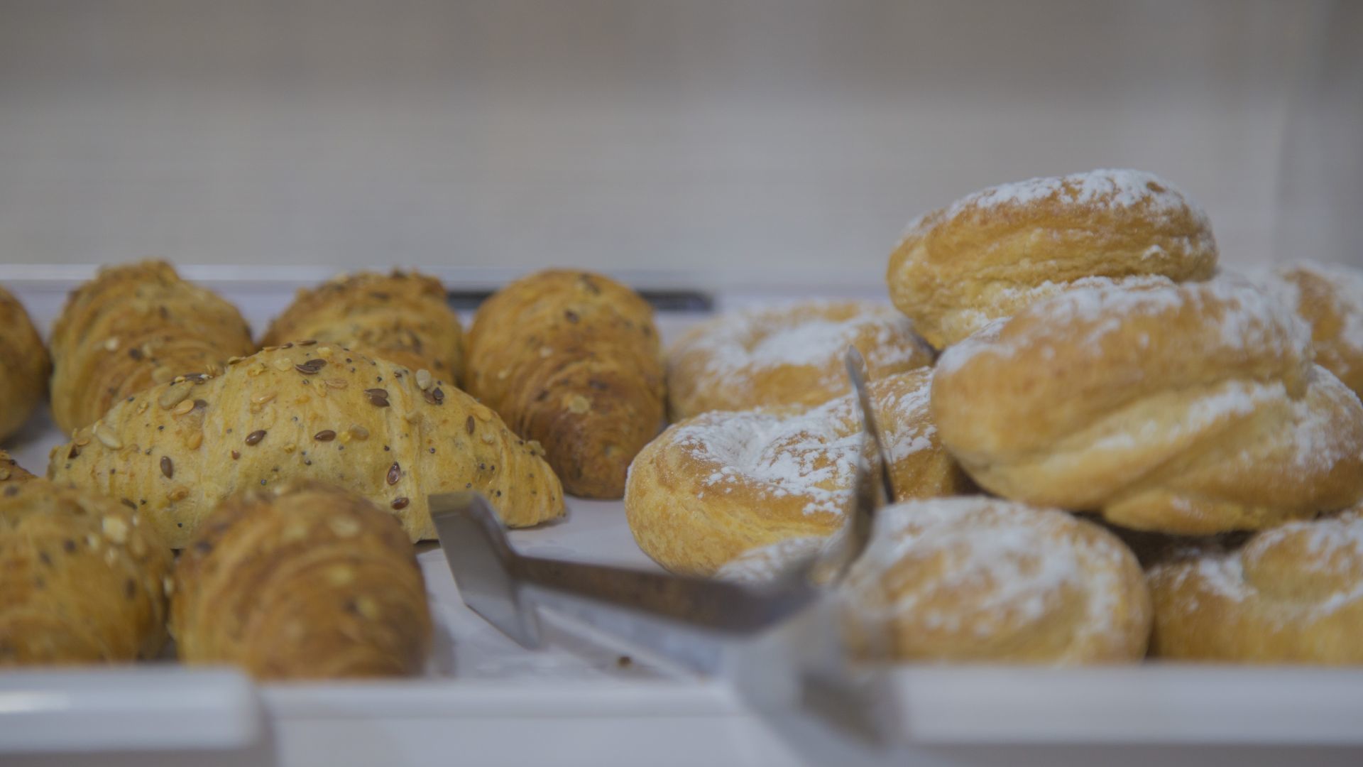 Verschiedene Backwaren, darunter Croissants und Brötchen, einige bestäubt mit Puderzucker.
