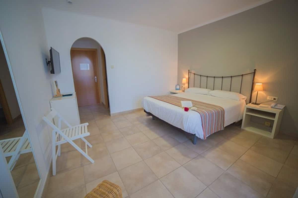 A bedroom with a bed, bedside tables, a chair, and a TV mounted on the wall.