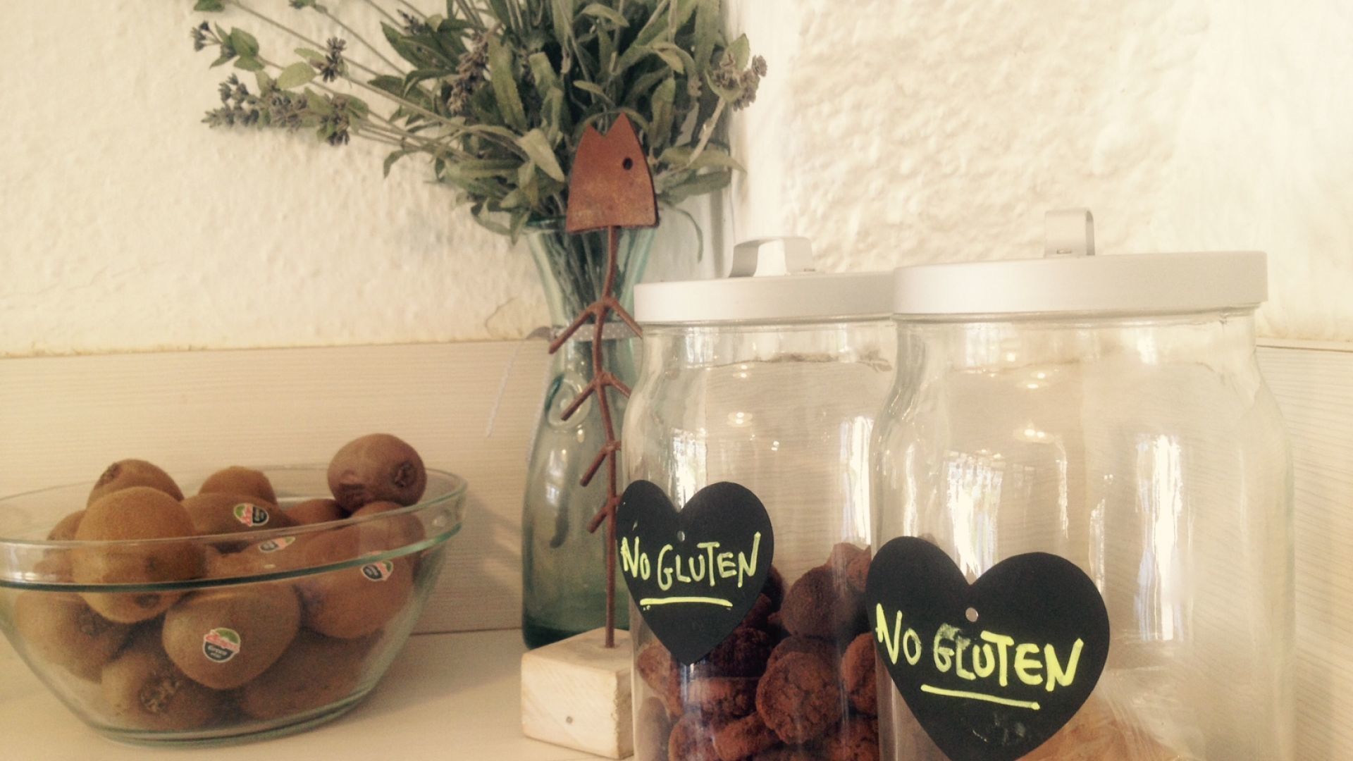 Dos frascos de vidrio con etiquetas que dicen "Sin Gluten", un cuenco de galletas y una planta decorativa.