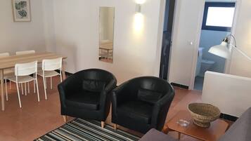 Een moderne woonkamer met een bank, twee zwarte lederen fauteuils, een eettafel met stoelen, een gestreept vloerkleed, een klein houten bijzettafeltje met een schaal, en een spiegel aan de muur.