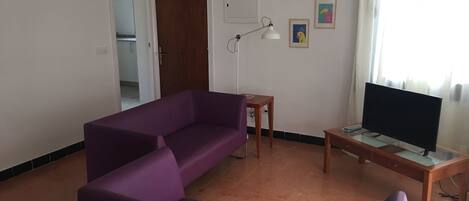A living room with a purple sofa, a small wooden table with a TV, and a floor lamp.