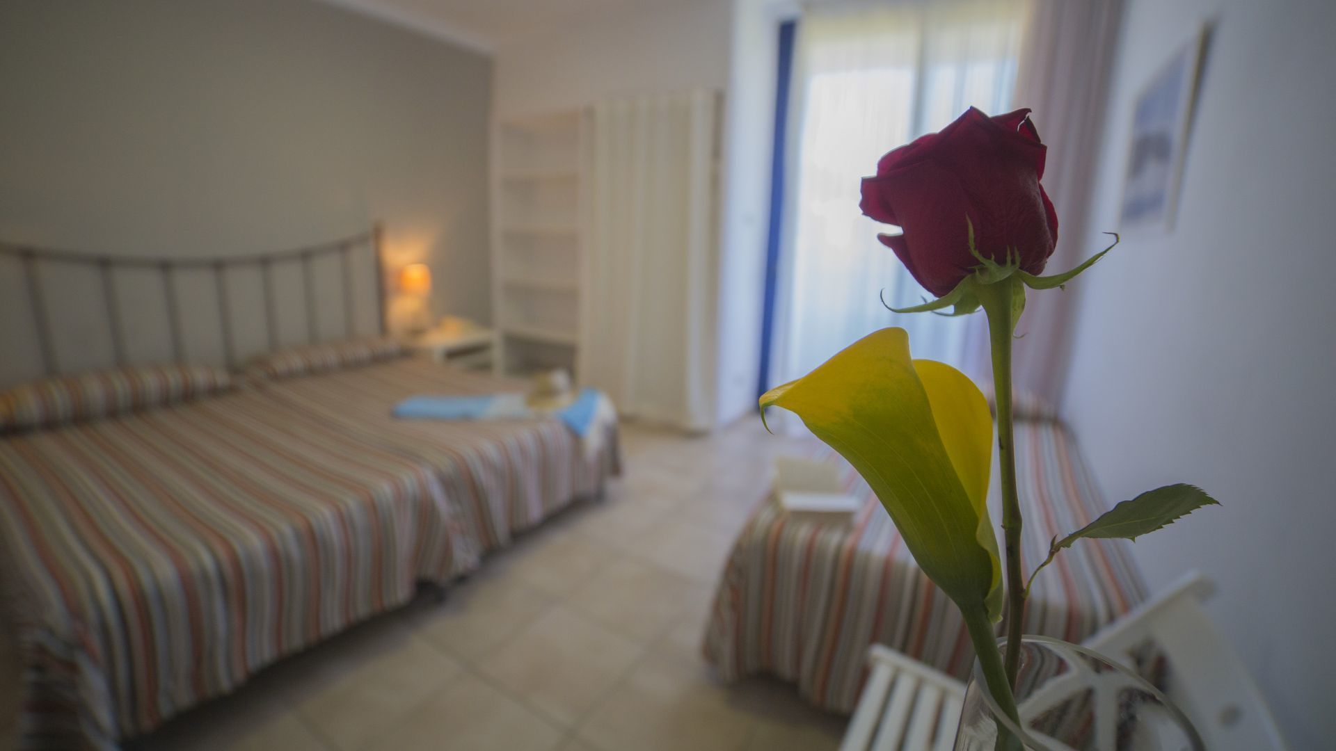 A bedroom with a bed, bedside table, and a single rose in a vase.