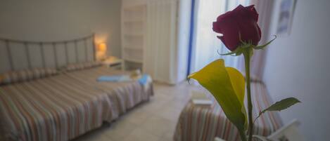 A bedroom with a bed, bedside table, and a single rose in a vase.