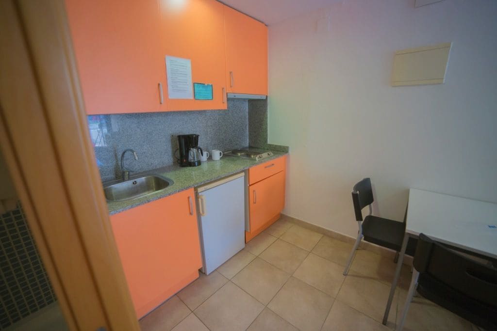 A compact kitchen with orange cabinets, a white refrigerator, a sink, and a coffee maker.