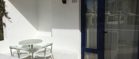 A white exterior wall with a number '005' sign, a glass door, and a small round table with two chairs.