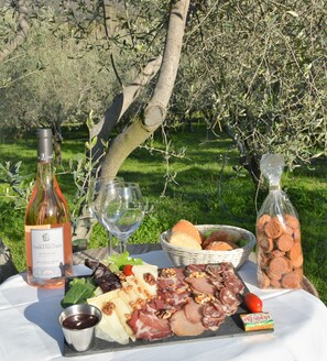 A picnic setup with a wine bottle, glasses, a basket of bread, a cheese board, and a bottle of nuts. - Camping Le Sagone (Vico)