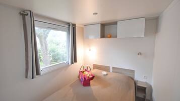 Une chambre à coucher avec un lit, une fenêtre avec des rideaux, une table de chevet et une étagère fixée au mur, sur laquelle se trouve un petit objet orange.