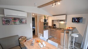 A modern kitchen with a dining area, a TV mounted on the wall, and a small refrigerator. - Camping Le Sagone (Vico)