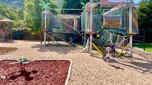 A playground with climbing structures and a slide, surrounded by a sandy area and trees. - Camping Le Sagone (Vico)