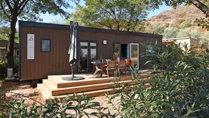 A modern cabin with a wooden deck, a dining area with outdoor furniture, and a large window. - Camping Le Sagone (Vico)