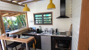 Een compacte keuken met een spoelbak, fornuis en vaatwasser, een klein eetgedeelte met krukjes, en een raam met uitzicht op groen.