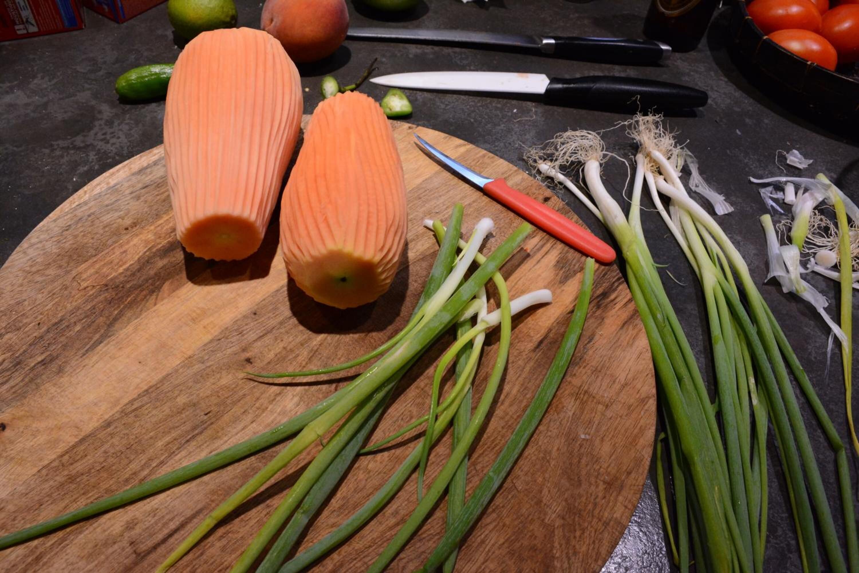 A wooden cutting board with julienned carrots, green onions, and a knife on a kitchen counter.