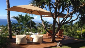 Een houten terras met tuinmeubilair, een grote parasol en uitzicht op de oceaan.