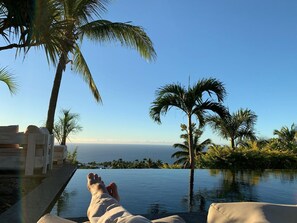 Une personne se détend au bord d’une piscine à débordement, avec vue sur l’océan et les palmiers.