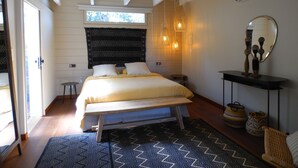Een slaapkamer met een bed, een plafondventilator, een raam, een nachtkastje, een spiegel en een wandairconditioner.