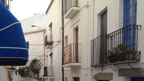 A narrow cobblestone street flanked by white buildings with blue doors and balconies. - Hostal Vehí (Cadaqués)