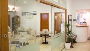 A cafe with a wooden counter, a reception desk, and a dining area with tables and chairs. - Hostal Vehí (Cadaqués)