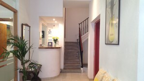 A reception area with a reception desk, a staircase, a potted plant, and a sofa with patterned cushions. - Hostal Vehí (Cadaqués)
