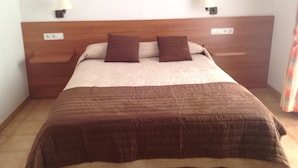 A bed with a wooden headboard, two bedside tables, and two wall-mounted lamps. - Hostal Vehí (Cadaqués)