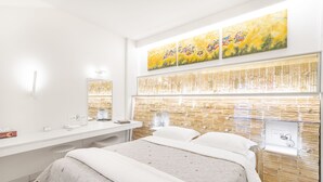 Una habitación de hotel moderna con una cama grande, una tocador amplia con espejo y una obra de arte colgada en la pared.