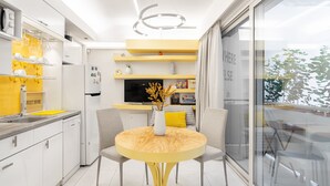 Una cocina moderna con armarios blancos, un comedor amarillo y un amplio ventanal con vistas a zonas verdes.